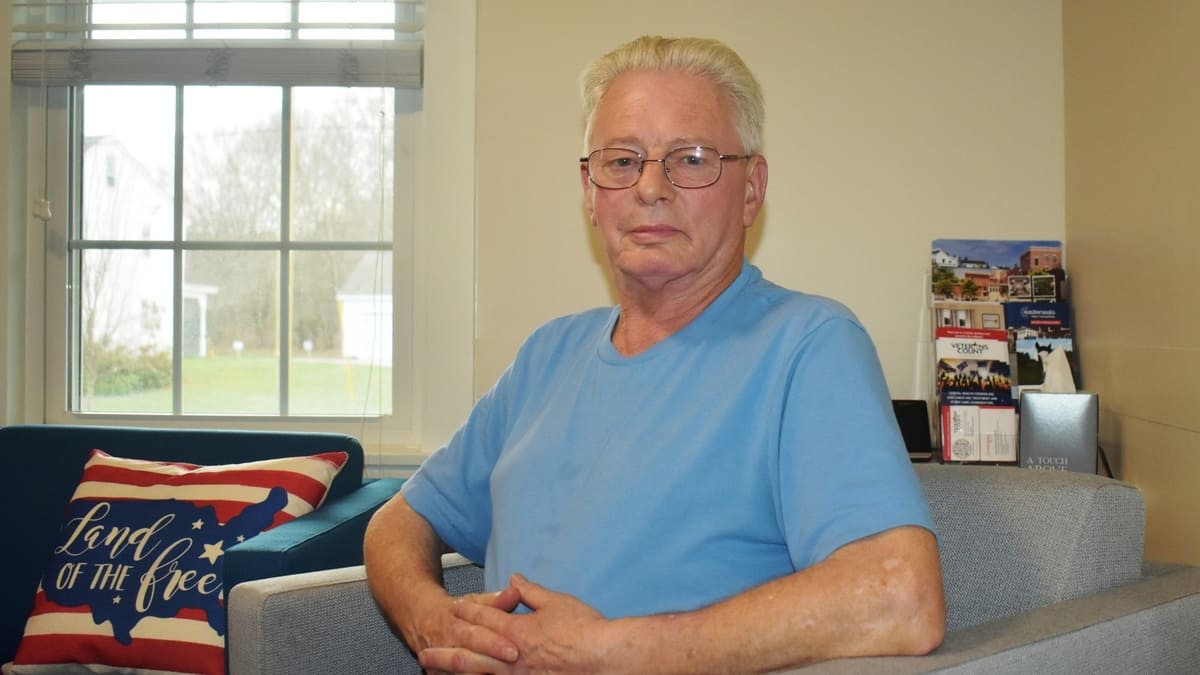 Man in light blue t-shirt sittings in a gray chair.